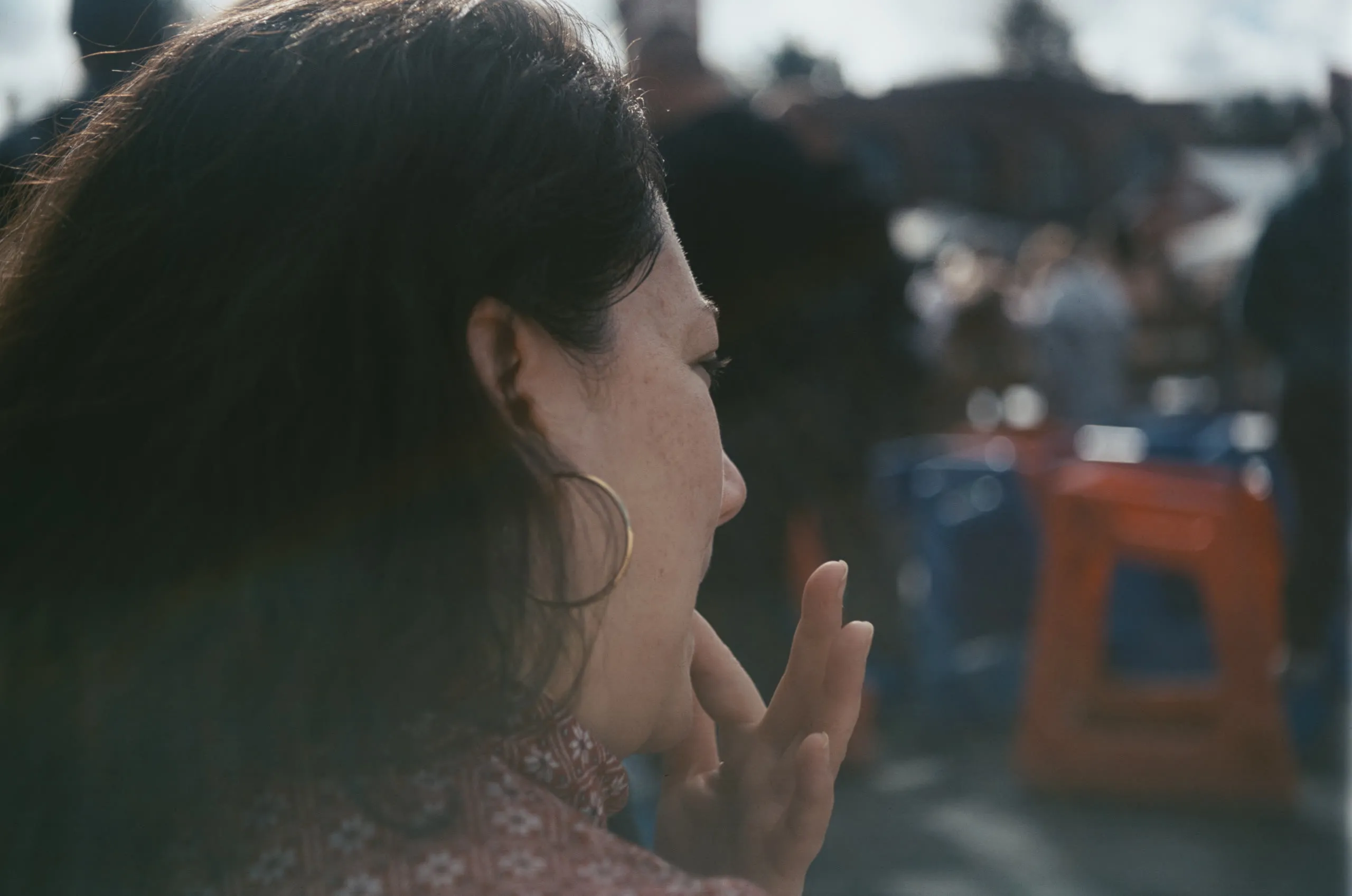 Backlit profile of a woman with hoop earrings at an outdoor gathering