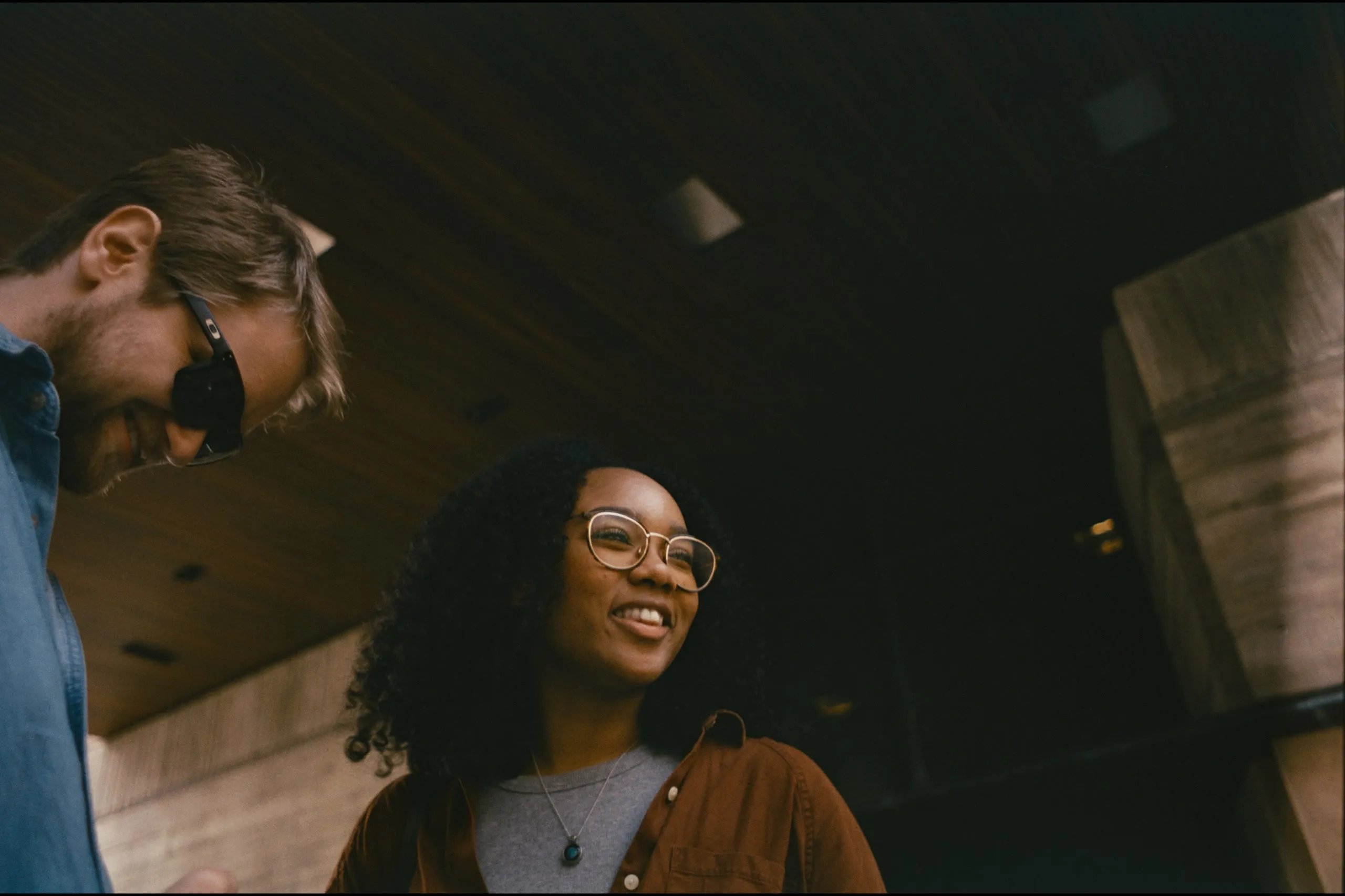 Two friends laughing together under a dark overhang, warm light on their faces