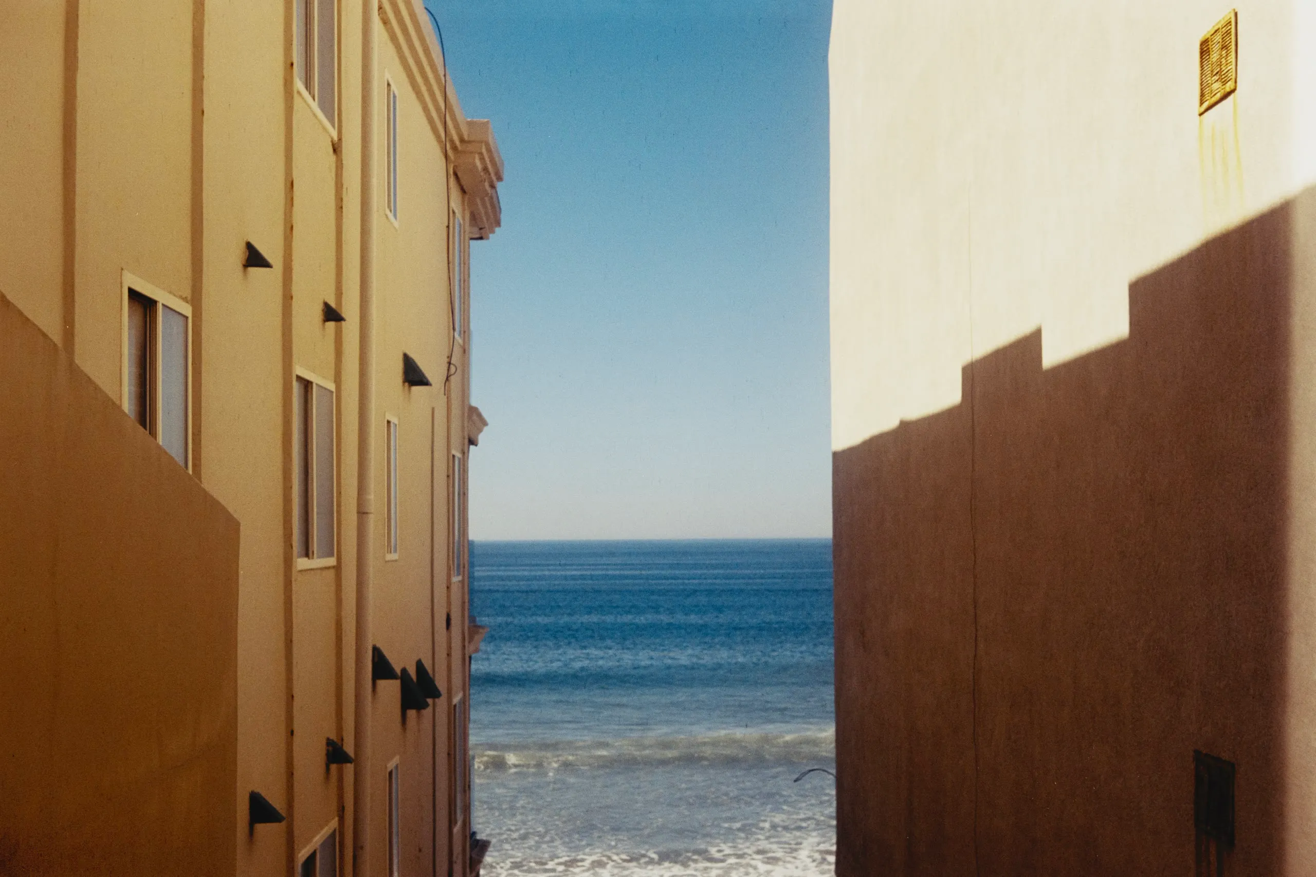 The ocean framed in the gap between two pale stucco buildings